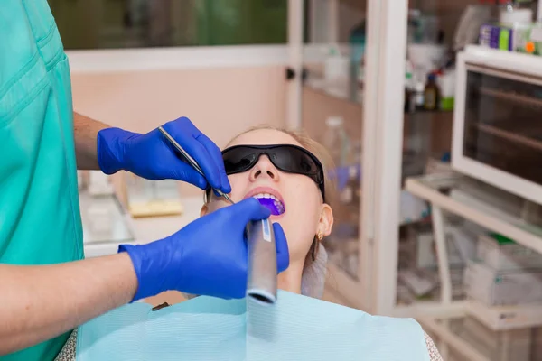 El dentista utiliza una lámpara UV dental en los dientes del paciente — Foto de Stock