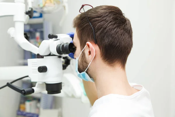 Homem dentista está olhando através de um microscópio — Fotografia de Stock