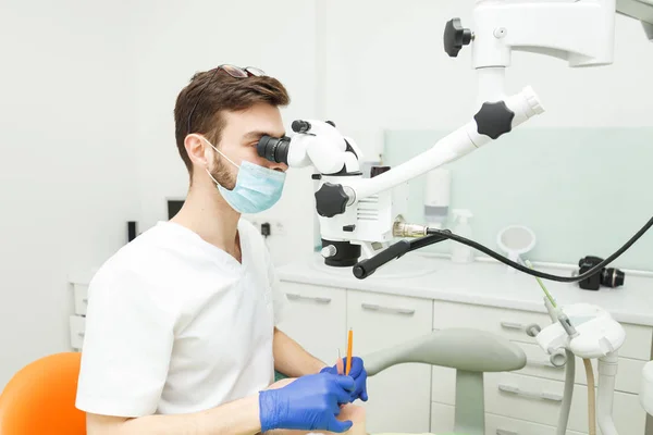 Homem dentista está olhando através de um microscópio — Fotografia de Stock