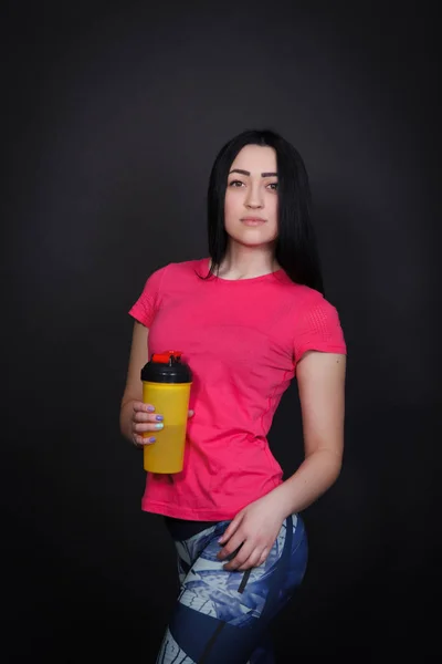 Sporty woman holding a shaker. Woman on a black background in sportswear — Stock Photo, Image
