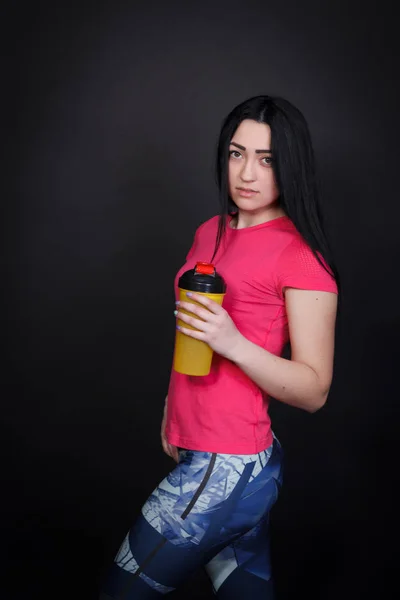Sporty woman holding a shaker. Woman on a black background in sportswear — Stock Photo, Image