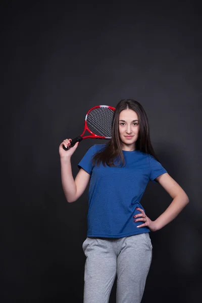 Jovem desportiva com uma raquete de ténis. Mulher em um fundo preto — Fotografia de Stock