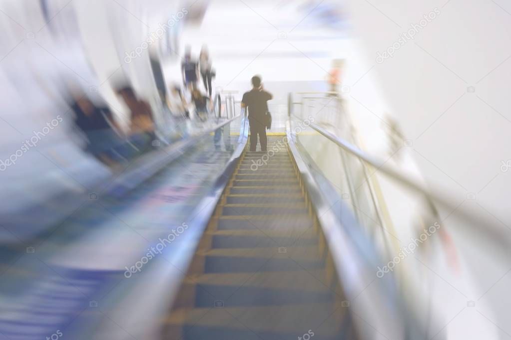 Motion Blurred Image of Man Hoding Moblie Phone and Standing on Escalator.