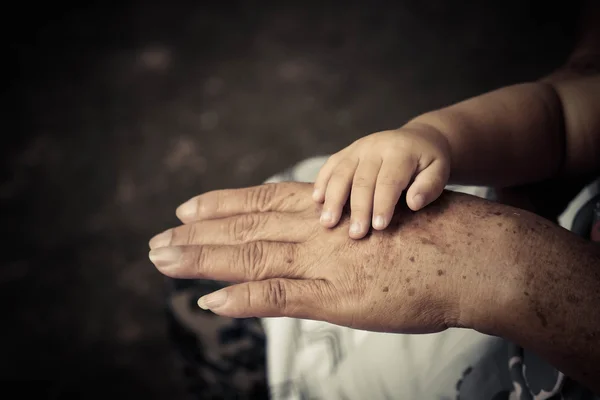 Gammal kvinnlig hand håller ung baby hand — Stockfoto