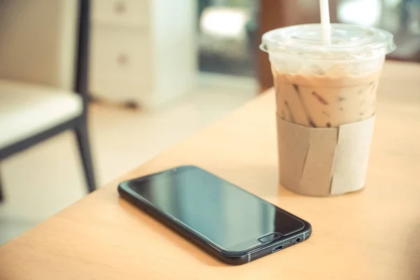 Un smartphone negro y un vaso de café helado — Foto de Stock