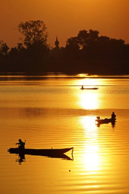 Ubon Ratchathani 'de gündoğumu silueti olan teknelerdeki balıkçılar                                