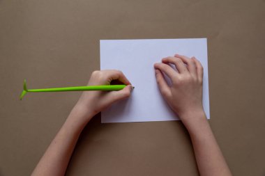 Solak bir çocuk açık yeşil bir kalemle beyaz kağıda kağıt arka planda yazı yazıyor. en üstteki görünüm