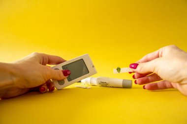 Diyabet. Tıbbi ekipman. Tıbbi konsept. Kan şekeri seviyesini Glikoz sayacına göre ölçmek için kadın ellerini parmağında mızrak kullanarak sarı arkaplanda kapat 