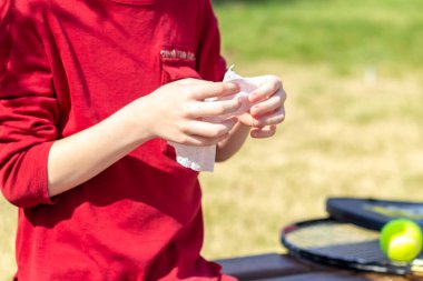 Kırmızı tişörtlü çocuk ellerini antibakteriyel mendille temizliyor. Açık hava önleme kavramı