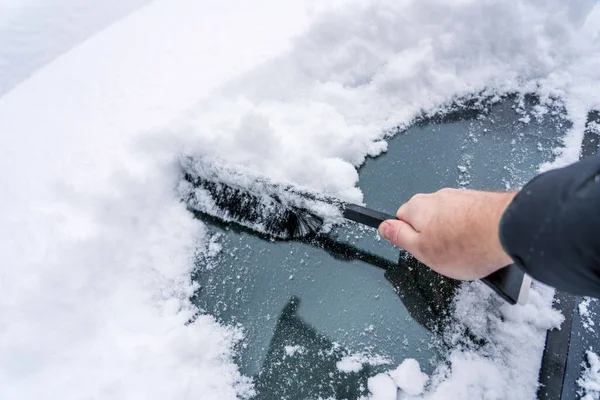 Hand are holding and brushing car window clean of snow. car covered in snow during heavy snow fall. Winter and seasonal concept.