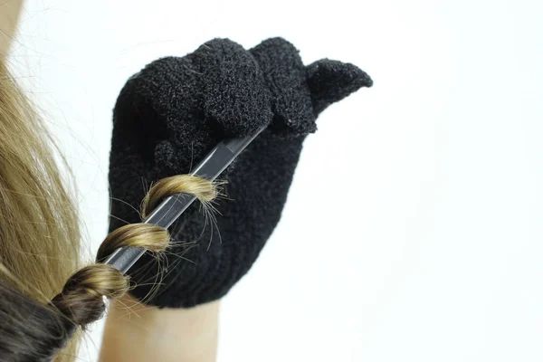 A woman in thermal gloves makes her hair curl with Curling iron — Stock Photo, Image