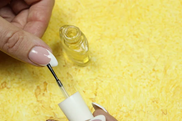 Women's hands make nail Polish on a yellow background. Beauty, the concept of the manicure