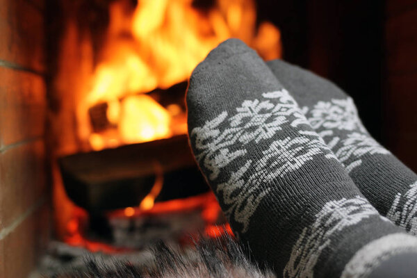 A woman warms her feet in knitted socks by the fireplace on a winter evening