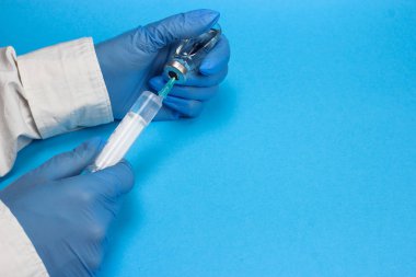 Sağlık çalışanı aşıyı şırıngaya çeviriyor. Mavi arkaplan