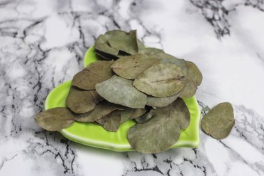 Kurumuş okaliptüs yaprakları yeşil bir tabakta mermer bir arka planda.
