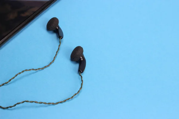 in ear headphones and smartphone on blue background