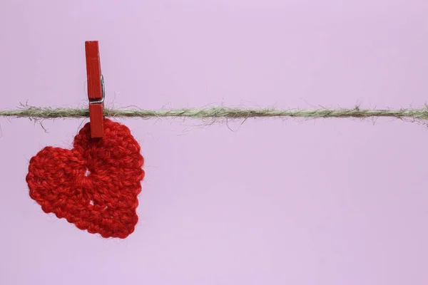 Вязаное сердце висит на бельевой верёвке, розовый фон, место для текста — стоковое фото
