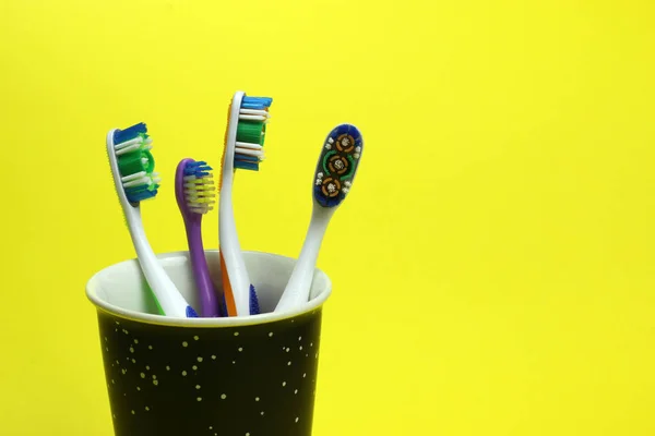 Four toothbrushes in a glass on a yellow background — Stock Photo, Image