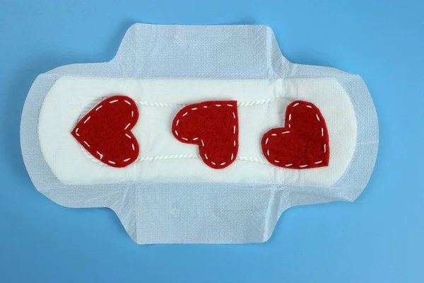 Санитарная прокладка с красными сердцами на синем. Личная гигиена, понятие женской гигиены. Критические дни, период крови, менструальный цикл . — стоковое фото