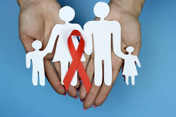 Červená stuha a řezání papírové rodiny do ženských rukou. Symbol povědomí o AIDS. — Stock fotografie