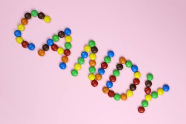 Şekerleme kelimesi pembe bir arka planda renkli şekerler tarafından içerir.