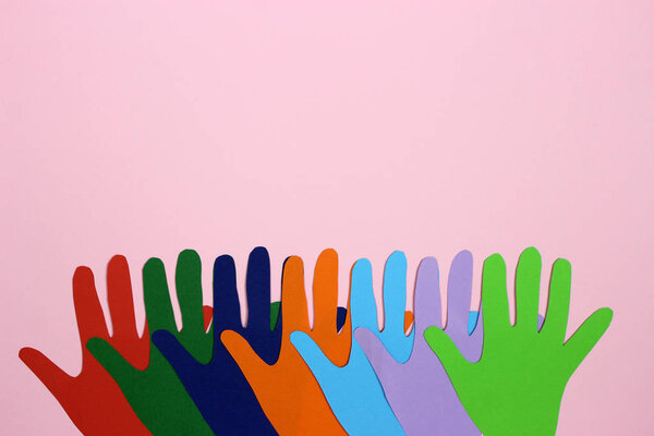 Multicolored paper hands on a pink background. Space for text