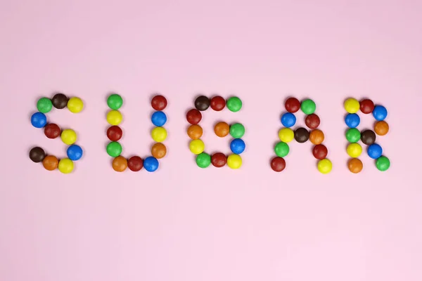 Pembe arka planda, renkli şekerlerden şeker kelimesi — Stok fotoğraf