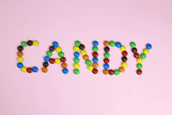 Şekerleme kelimesi pembe bir arka planda renkli şekerler tarafından içerir. — Stok fotoğraf