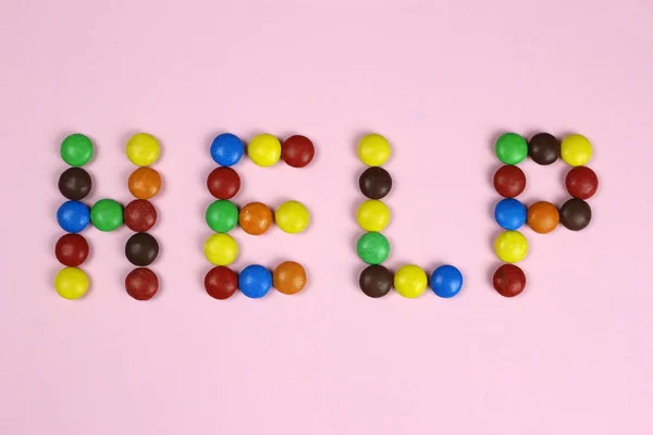 Word aiuto di caramelle multicolore su sfondo rosa — Foto Stock