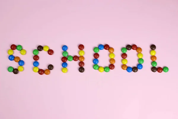 Word School van gekleurde snoepjes op een roze achtergrond — Stockfoto