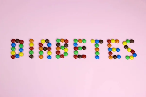 Słowo cukrzyca wielokolorowe cukierki na różowym tle — Zdjęcie stockowe