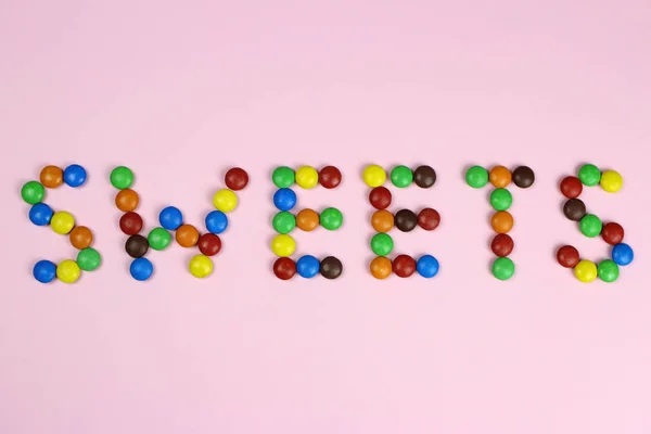 Słowo słodycze są zawarte przez kolorowe cukierki na różowym tle — Zdjęcie stockowe