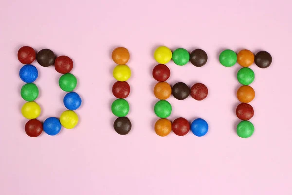 Dieta di parola di caramelle multicolori su sfondo rosa — Foto Stock