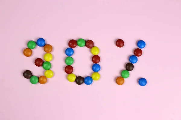 Trenta per cento di caramelle colorate su uno sfondo rosa — Foto Stock