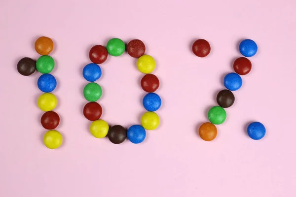 Dziesięć procent kolorowych cukierków na różowym tle — Zdjęcie stockowe