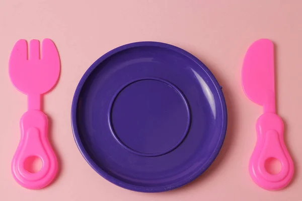 plastic toys tableware plate, fork, knife on pink background