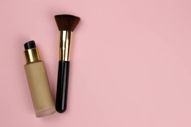 Foundation in a glass bubble and a makeup brush on a pink background