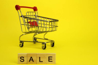 Mini supermarket cart, trolley on a yellow background. Purchases. The Word Sale
