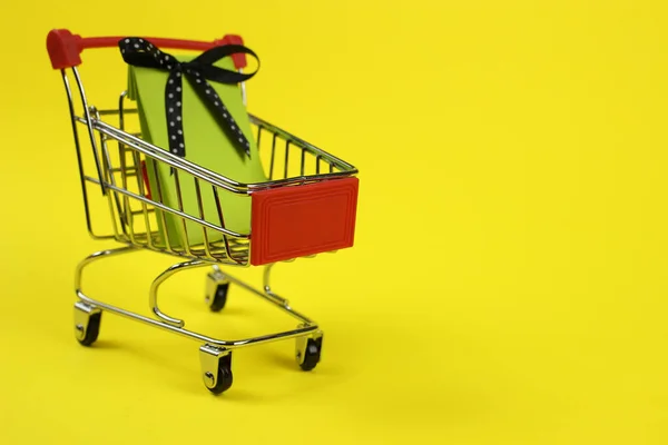 Mini carrinho de supermercado, carrinho com presente em um fundo amarelo. Compras — Fotografia de Stock