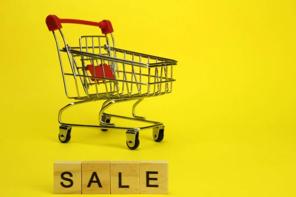 Mini carrinho de supermercado, carrinho com fundo amarelo. Compras. A venda da palavra — Fotografia de Stock