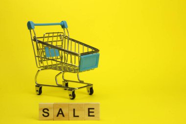Mini supermarket cart, trolley on a yellow background. Purchases. The Word Sale