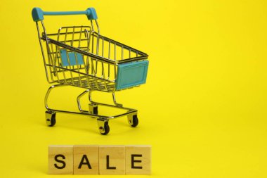 Mini supermarket cart, trolley on a yellow background. Purchases. The Word Sale