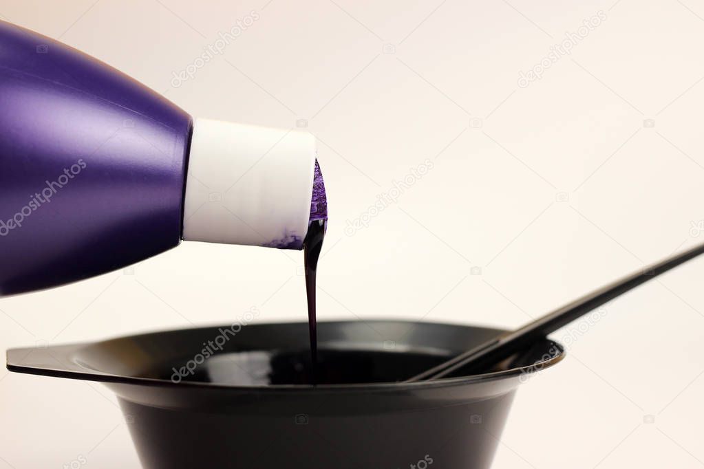 Hair dye is poured from a bottle into a bowl isolated on white