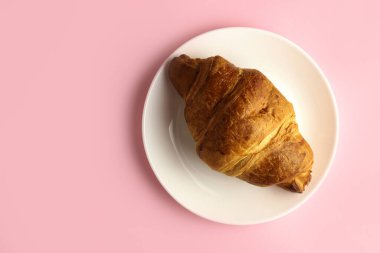 Pembe arka planda beyaz bir tabakta kruvasan.