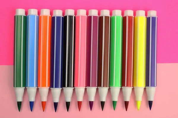 colored markers in a row on a pink background