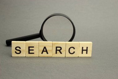 Sözcük Araması ahşap harflerden ve gri arka planda büyüteçten yapılmıştır.