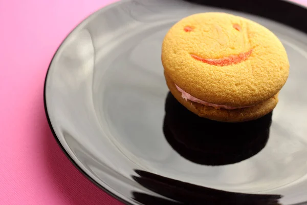 Smiley face cookies in a black plate on a pink background