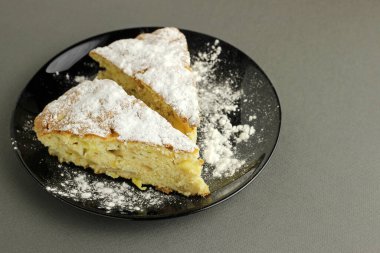 Lezzetli elmalı turta, Charlotte siyah bir arka planda siyah bir tabağa pudra şekeri serpiştirilmiş. Yan görünümü kapat.