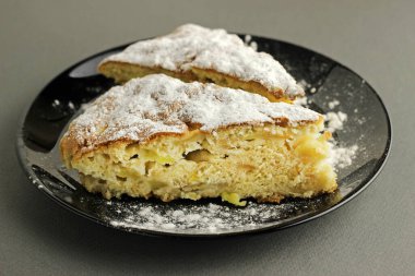 Lezzetli elmalı turta, Charlotte siyah bir arka planda siyah bir tabağa pudra şekeri serpiştirilmiş. Yan görünümü kapat.