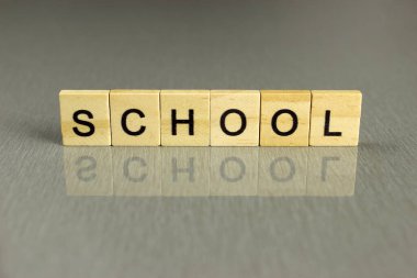 Kelime okulu gri bir arka planda kare tahta harflerden oluşur.